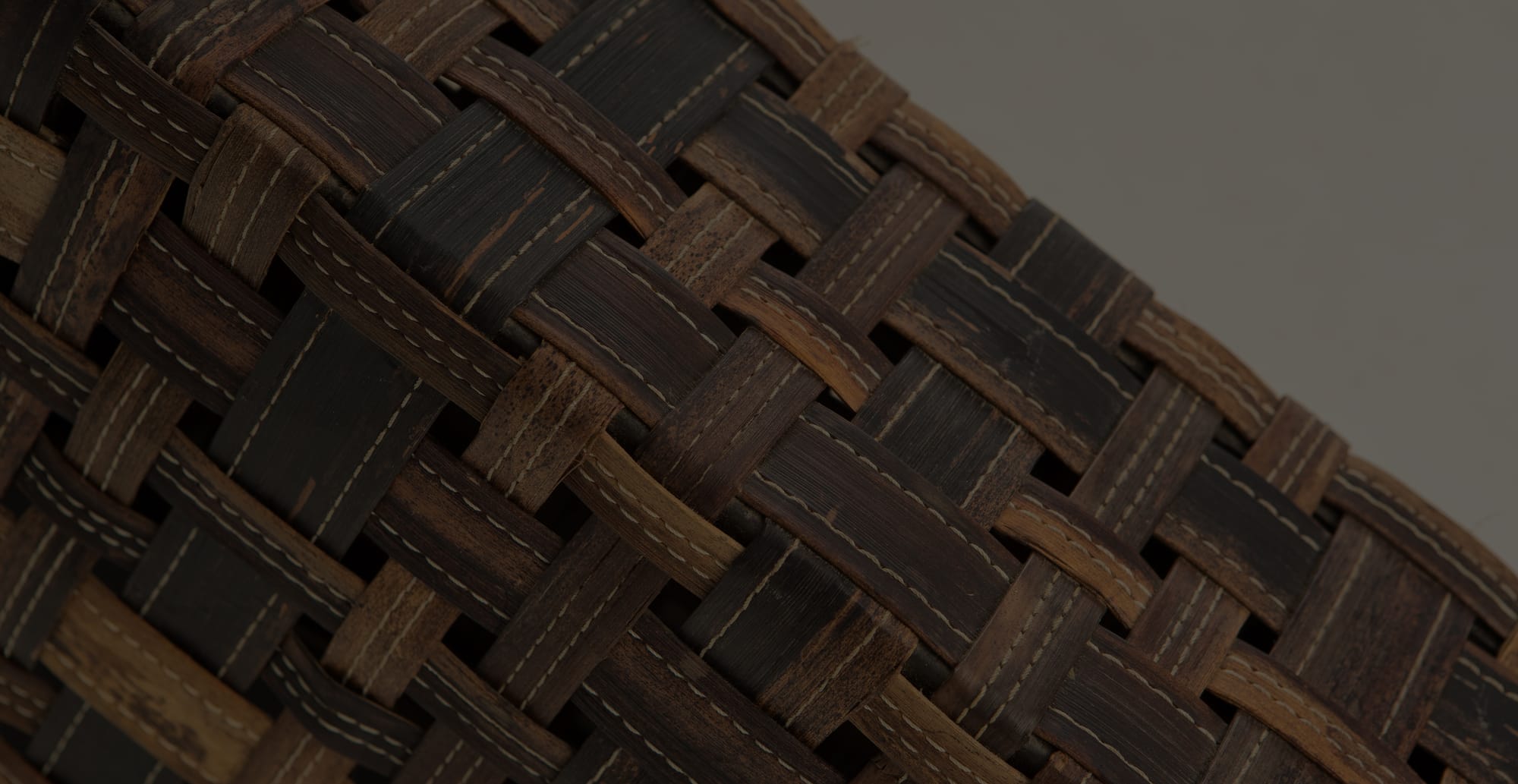 Detail of a basketweave panel in dark and honey-toned wood, stitched with pale thread