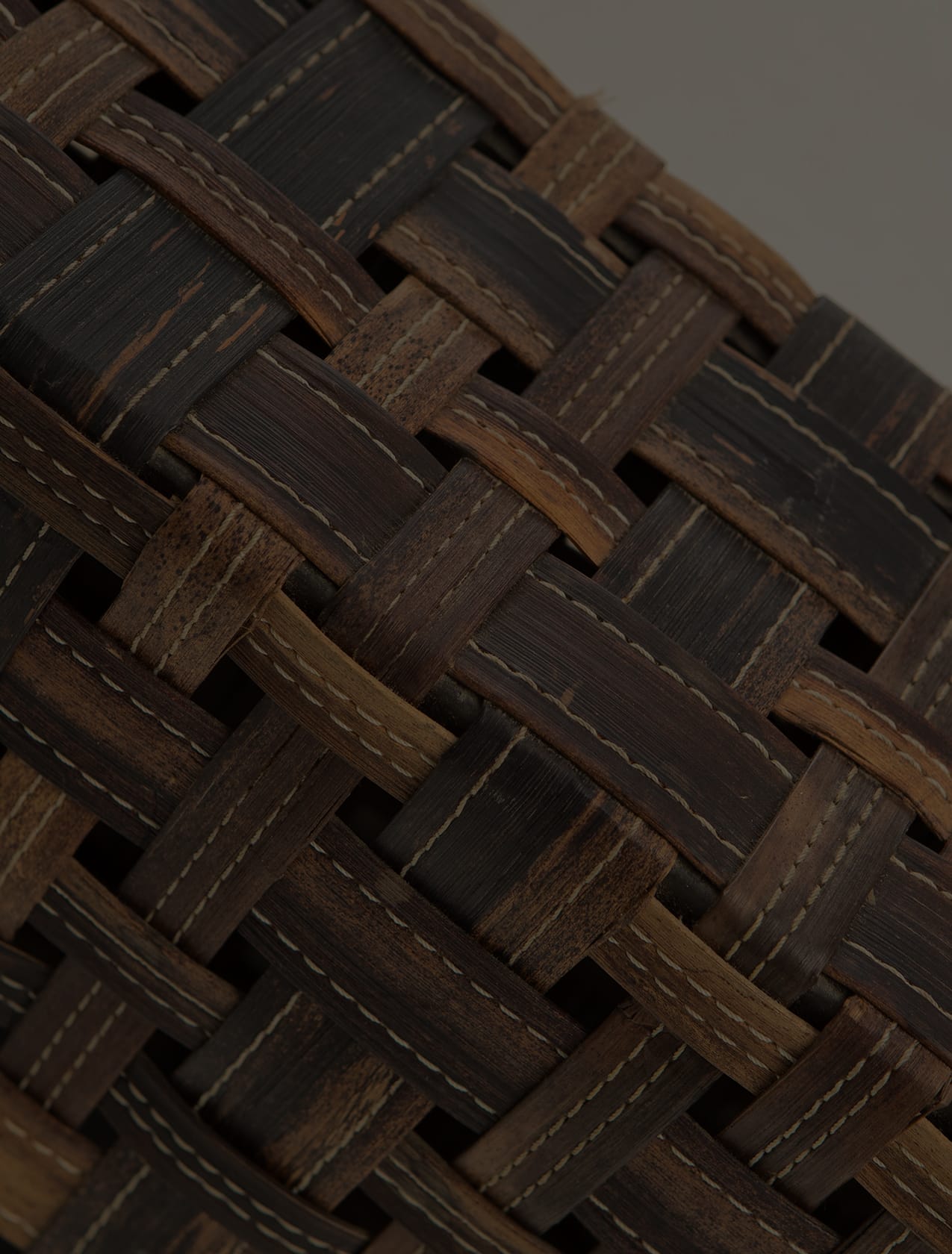 Detail of a basketweave panel in dark and honey-toned wood, stitched with pale thread